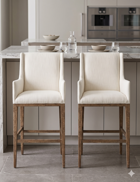 Banqueta alta de diseño contemporáneo con estructura de madera maciza en acabado natural. Presenta un asiento y respaldo integrado, tapizado en pana color claro con textura sutil. Incluye apoyapiés perimetral de madera para mayor estabilidad y confort