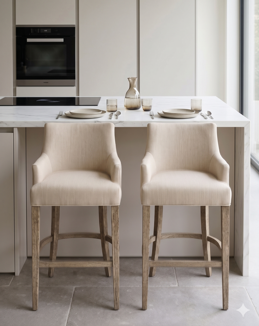 Banqueta alta de diseño contemporáneo con estructura de madera maciza en acabado natural. Presenta un asiento y respaldo integrado, tapizado en pana color claro con textura sutil. Incluye apoyapiés perimetral de madera para mayor estabilidad y confort