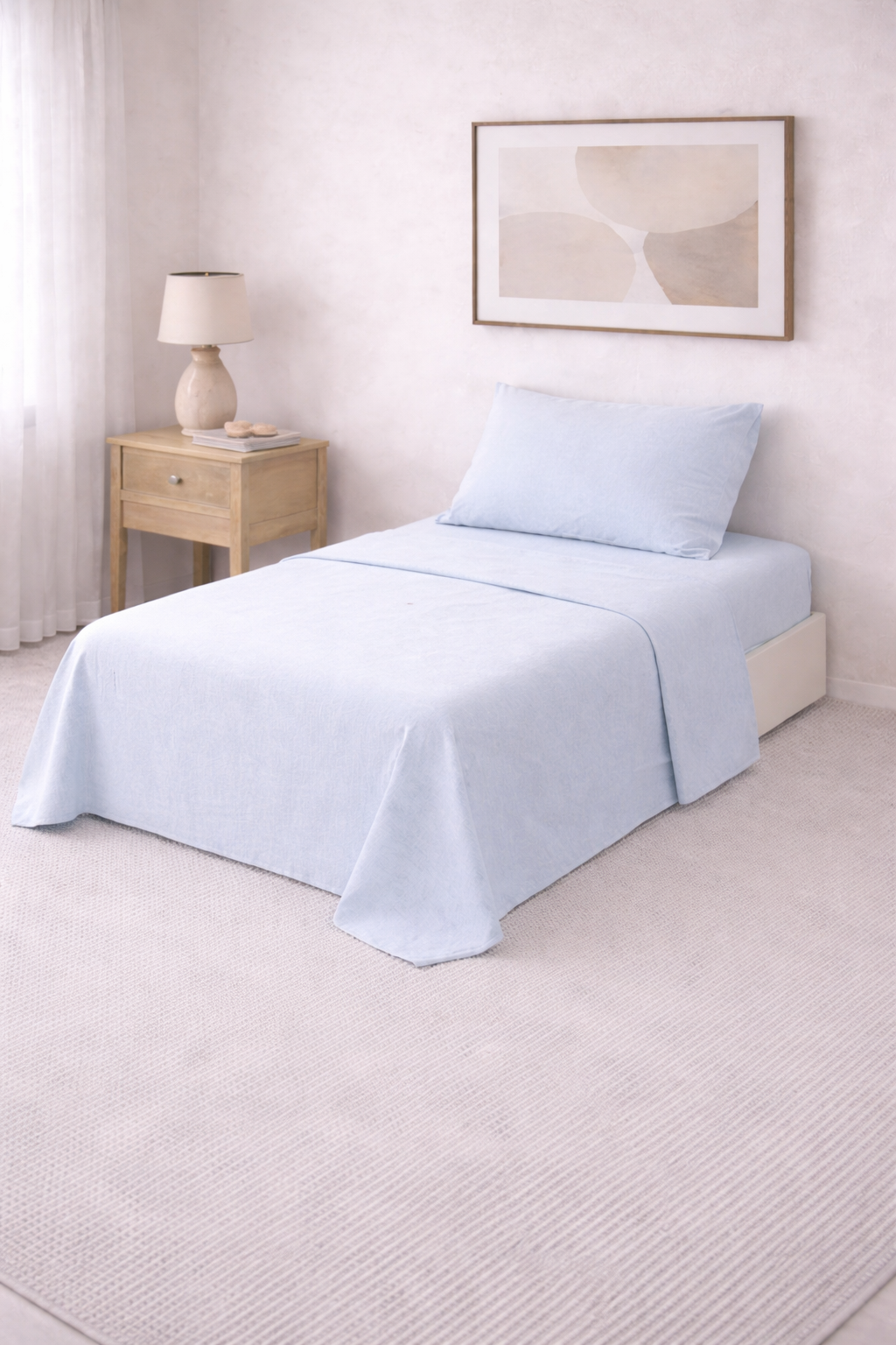 Cama de una plaza con sábanas lisas en tono suave, perfectamente tendida en un dormitorio luminoso de estilo minimalista con mesa de luz de madera y decoración neutra.
