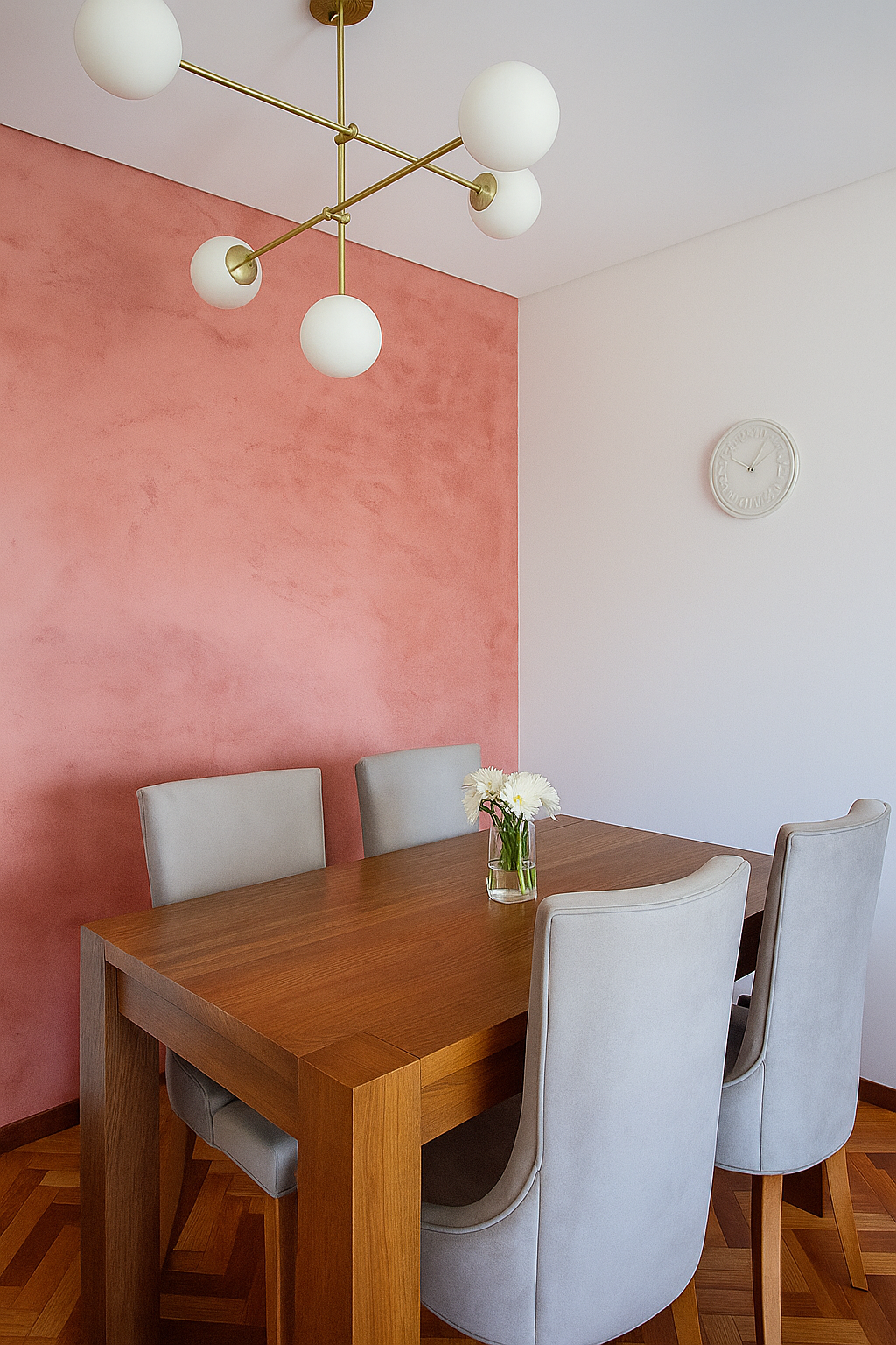 Comedor contemporáneo con pared de acento rosa, mesa de madera maciza, sillas tapizadas en gris claro y lámpara colgante moderna de esferas blancas. En la pared hay un espejo redondo sobre un mueble flotante gris.