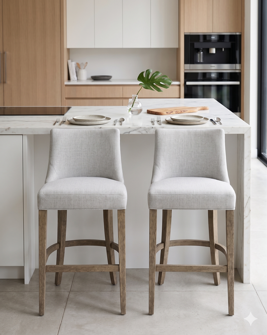 Banqueta alta de diseño contemporáneo con estructura de madera maciza en acabado natural. Presenta un asiento y respaldo integrado, tapizado en pana color claro con textura sutil. Incluye apoyapiés perimetral de madera para mayor estabilidad y confort