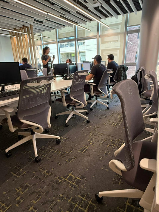 Oficina moderna equipada con sillas ergonómicas Aston en tonos neutros, con escritorios compartidos y diseño corporativo luminoso.