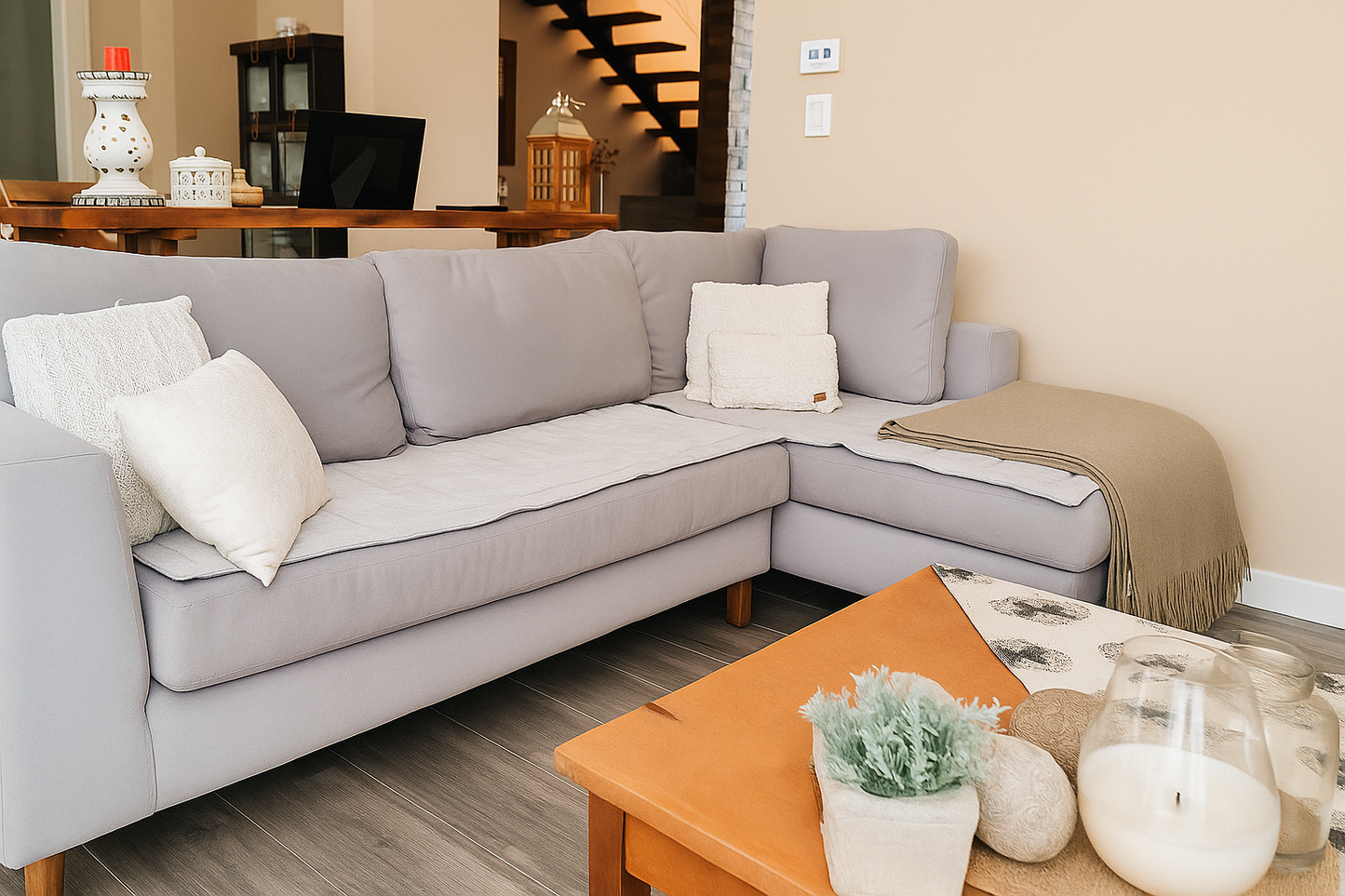 Un sillón de dos cuerpos en color gris claro, de diseño moderno y líneas rectas, se ubica en una sala iluminada por luz natural. Está decorado con cojines en tonos neutros, aportando comodidad y un estilo acogedor al ambiente