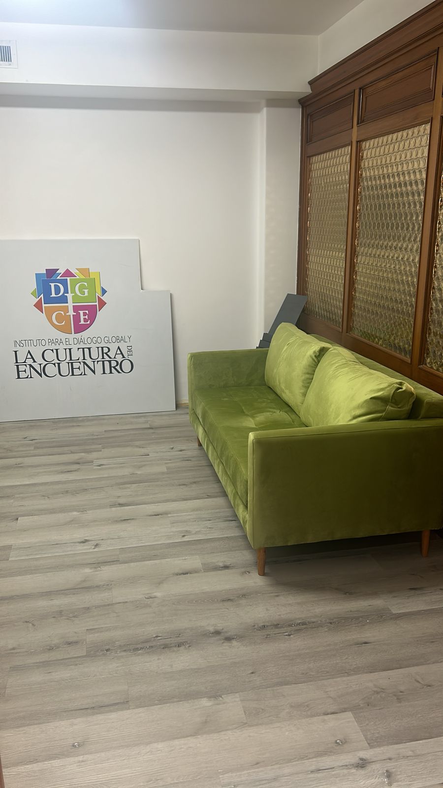 Sofá de tres cuerpos en tono verde, con diseño moderno y patas de madera, colocado en un ambiente interior con piso de madera clara.