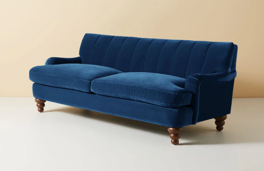 Vista completa del sofá modelo Malaika tapizado con respaldo vainillado profundo, brazos curvos y elegantes patas de madera oscura torneada, ubicado sobre fondo blanco, ideal para salas de estar, livings modernos o espacios clásicos que buscan un mueble llamativo y sofisticado.