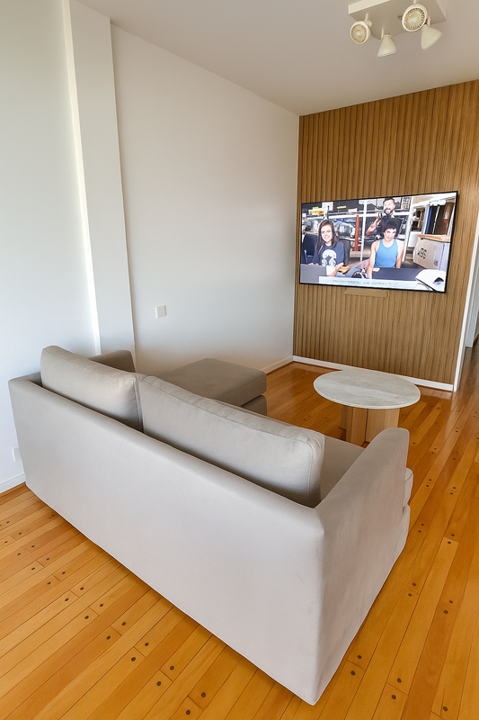 Sillón esquinero tapizado en tono beige, de líneas rectas y cojines amplios, ubicado sobre un piso de madera lustrada junto a una mesa ratona redonda de mármol.