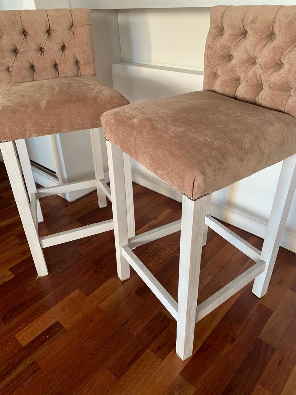 Dos Banquetas Altas Venet en tono nude, con respaldo capitoné, tachas en la base del asiento y patas blancas con travesaños, en la cocina de Antonia