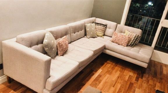 Esquinero beige capitoné a medida en el living de Silvia de noche, con el balcón iluminado de fondo