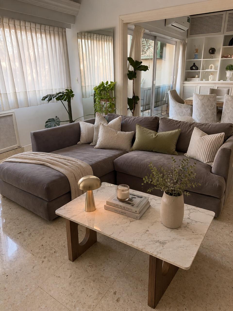 Esquinero Elton gris con chaise, almohadones verde oliva y a rayas y mesa de mármol, en el living de Naza Winograd