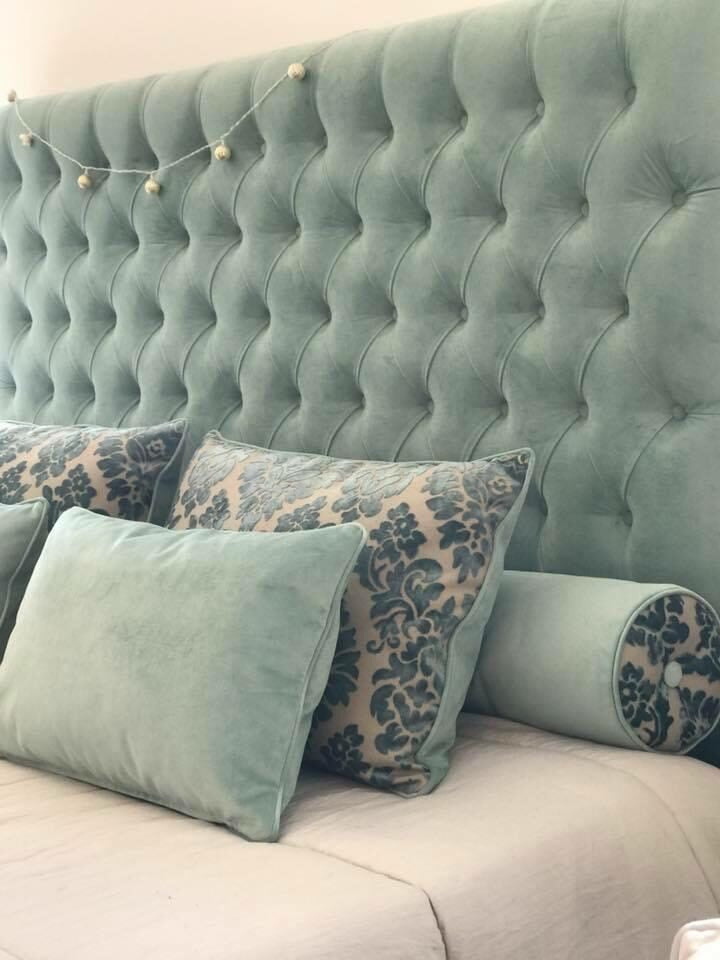 Respaldo Mily en terciopelo verde menta con capitoné en diamante, con almohadones al tono y de damasco azul, en el dormitorio de Araceli