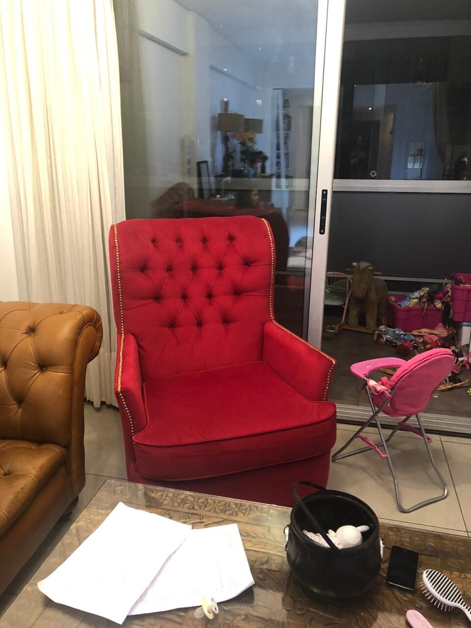 Sillón Esmeralda rojo con capitoné y tachas plateadas, junto al sofá Chesterfield caramelo del living de Gisela