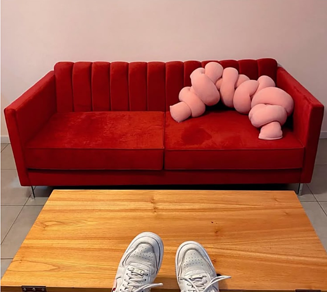 Sofá Mila rojo con respaldo acanalado vertical, almohadón rosa trenzado y mesa ratona de madera