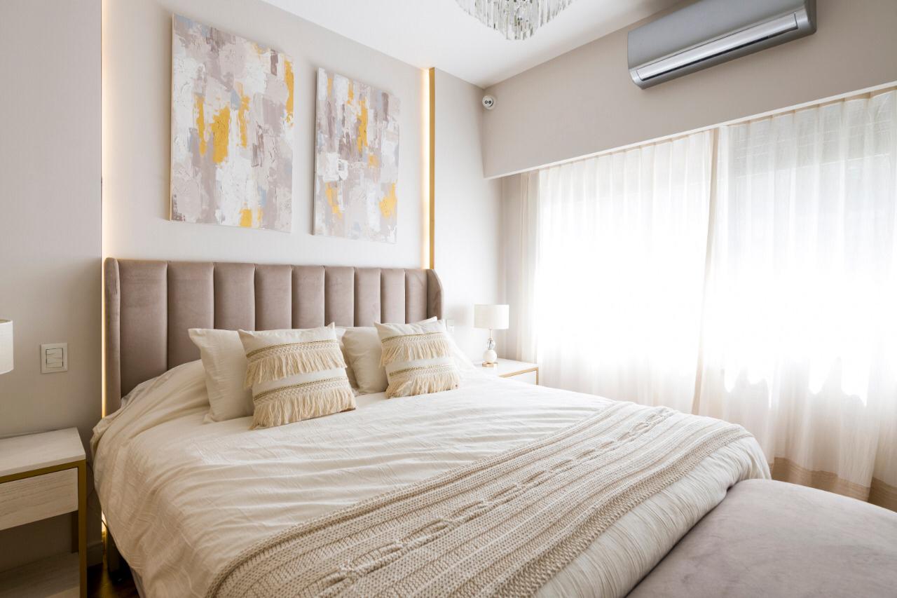 Respaldo de cama alto tapizado en tela beige, de diseño elegante y acolchado, que aporta calidez y sofisticación al dormitorio