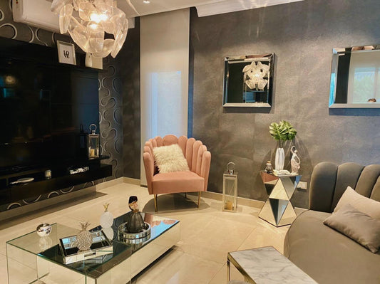 Ambiente elegante con un juego de sillones protagonistas: dos sillones individuales en tono rosa empolvado y un sofá alargado tapizado en gris, todos con un diseño de respaldo acanalado y patas doradas. La disposición de los sillones genera un espacio sofisticado y acogedor, ideal para reuniones o para destacar dentro de la decoración moderna