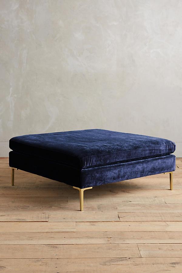 Banqueta rectangular tapizada en con patas doradas. Su diseño compacto y moderno la vuelve ideal para espacios reducidos o como apoya pies.