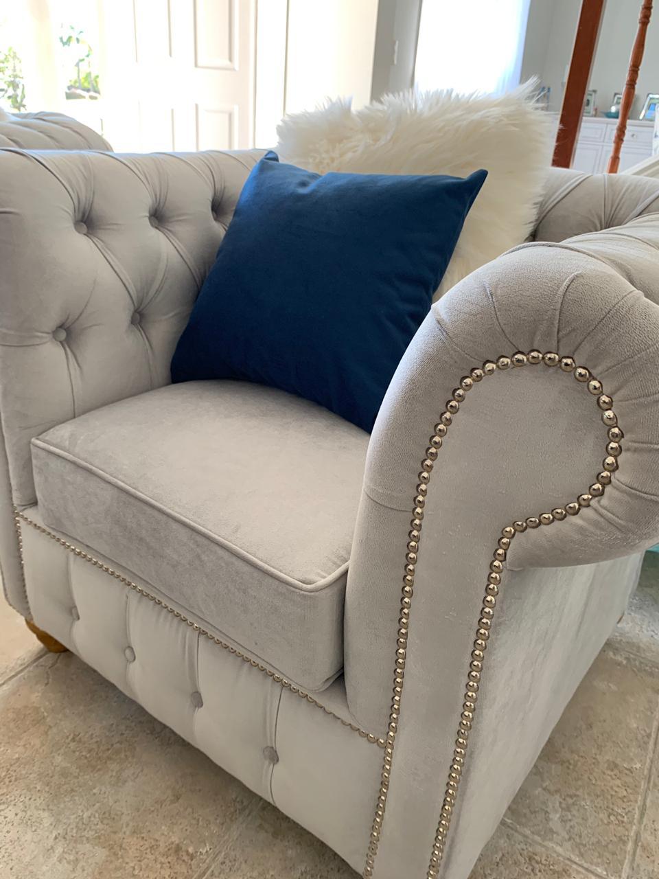 Juego de sillones con tapizado capitoné en tonos azul marino y gris, de diseño elegante y clásico, ubicados en un living luminoso con decoración sofisticada
