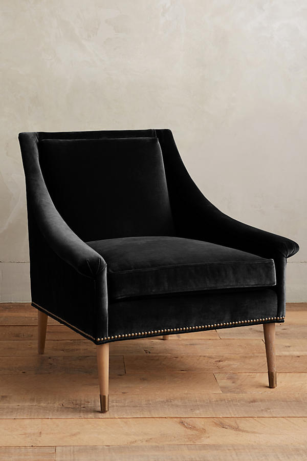 Sillón individual tapizado en negro, de líneas rectas con respaldo y asiento acolchados, brazos delgados y patas de madera rectas con detalle de tachas decorativas en la parte inferior.