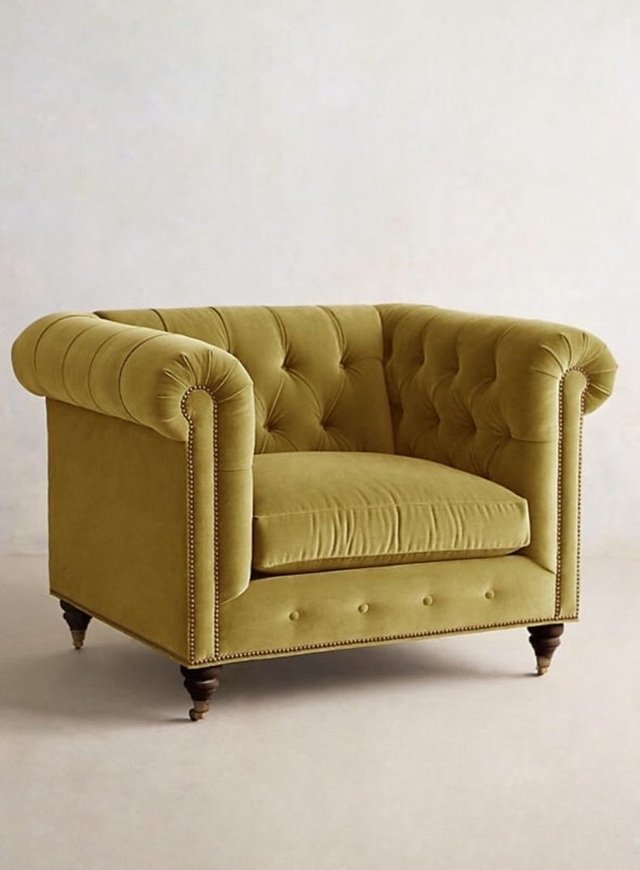 Sillón individual estilo Chesterfield tapizado en color amarillo, con capitoné en respaldo y apoyabrazos, tachas decorativas y patas de madera torneadas.