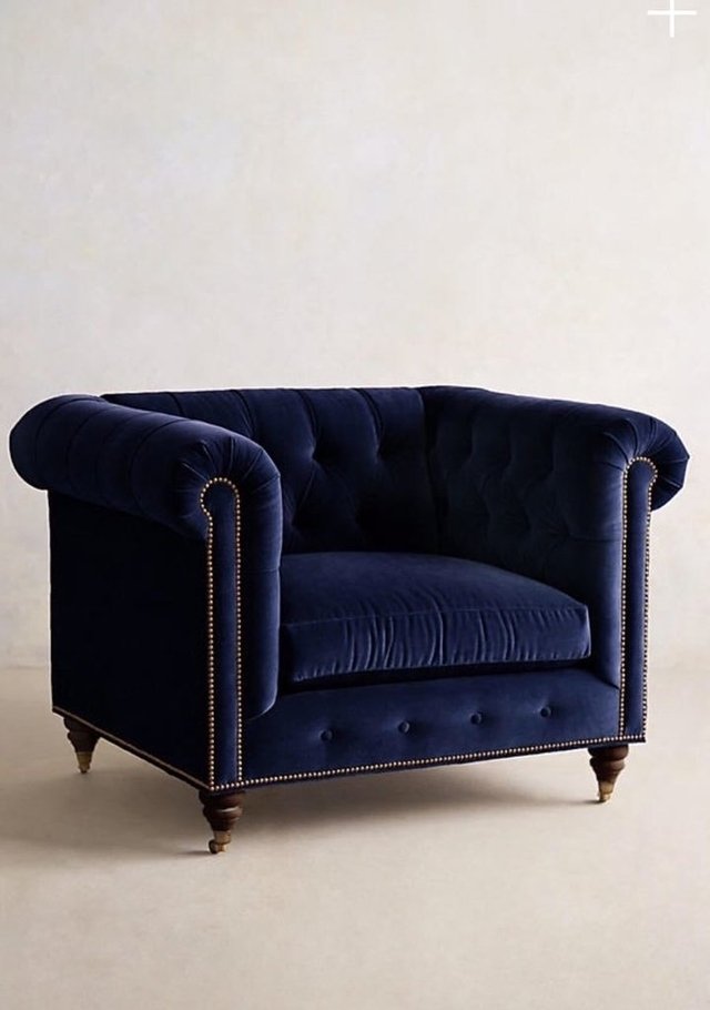 Sillón individual estilo Chesterfield tapizado en color azul, con capitoné en respaldo y apoyabrazos, tachas decorativas y patas de madera torneadas.