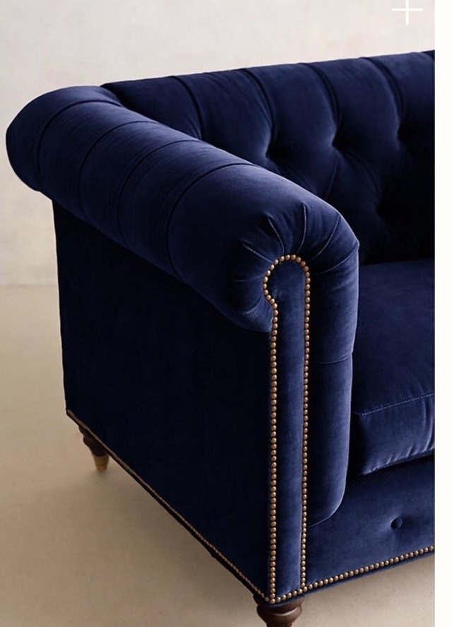 Sillón individual estilo Chesterfield tapizado en color azul, con capitoné en respaldo y apoyabrazos, tachas decorativas y patas de madera torneadas.