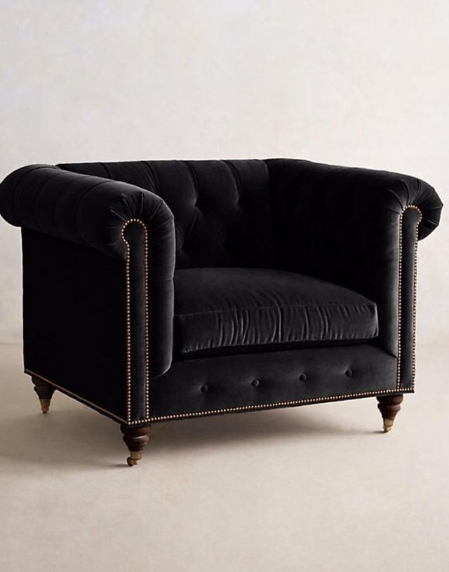 Sillón individual estilo Chesterfield tapizado en color negro, con capitoné en respaldo y apoyabrazos, tachas decorativas y patas de madera torneadas.