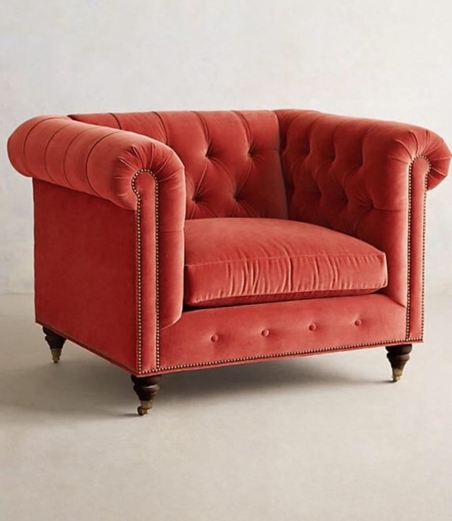 Sillón individual estilo Chesterfield tapizado en color rojo, con capitoné en respaldo y apoyabrazos, tachas decorativas y patas de madera torneadas.
