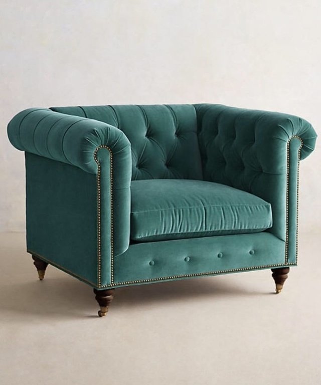 Sillón individual estilo Chesterfield tapizado en color verde agua, con capitoné en respaldo y apoyabrazos, tachas decorativas y patas de madera torneadas.
