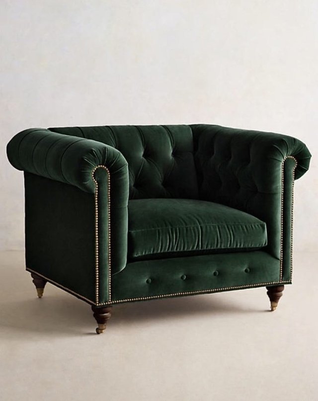 Sillón individual estilo Chesterfield tapizado en color verde, con capitoné en respaldo y apoyabrazos, tachas decorativas y patas de madera torneadas.