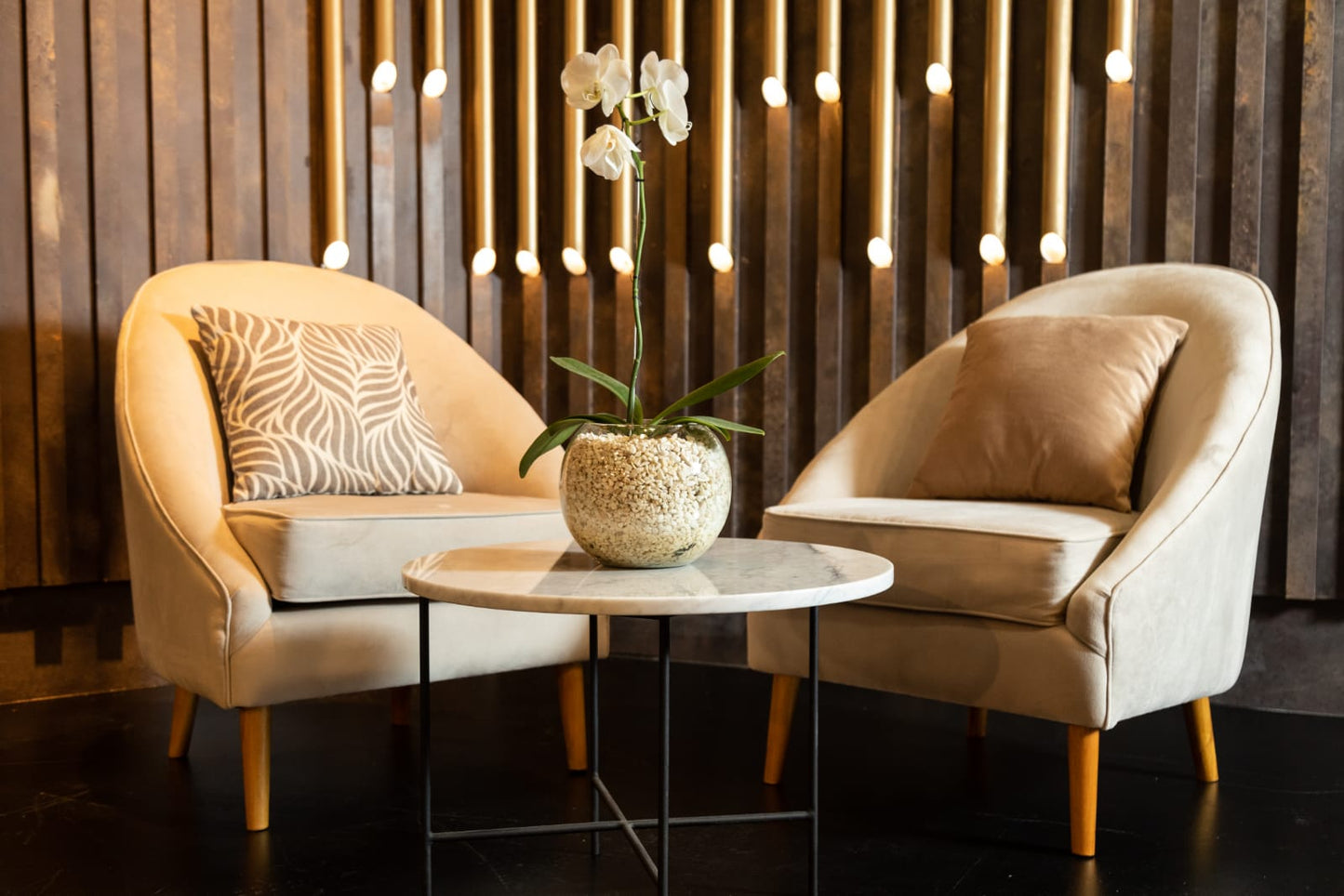 Par de sillones individuales tapizados en tono beige con patas de madera, de diseño moderno y respaldo curvo, decorados con almohadones a tono, ideales para un ambiente elegante y acogedor