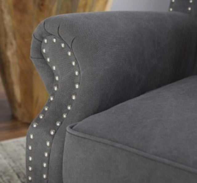 Sillón estilo clásico tapizado en color gris oscuro, con respaldo capitoné alto, orejas curvas, apoyabrazos redondeados y tachas decorativas, patas de madera talladas