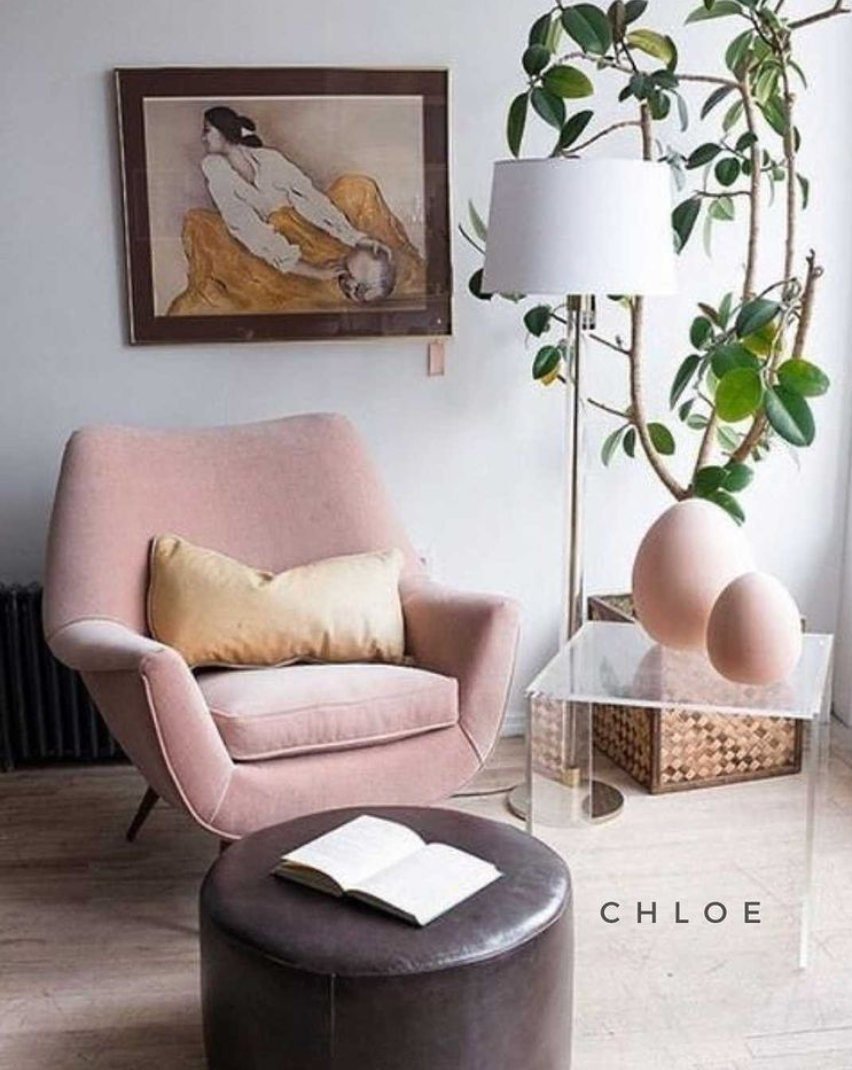 Sillón individual tapizado en tela rosa claro, de diseño retro con respaldo curvo envolvente, asiento acolchonado y patas de madera inclinadas estilo escandinavo.