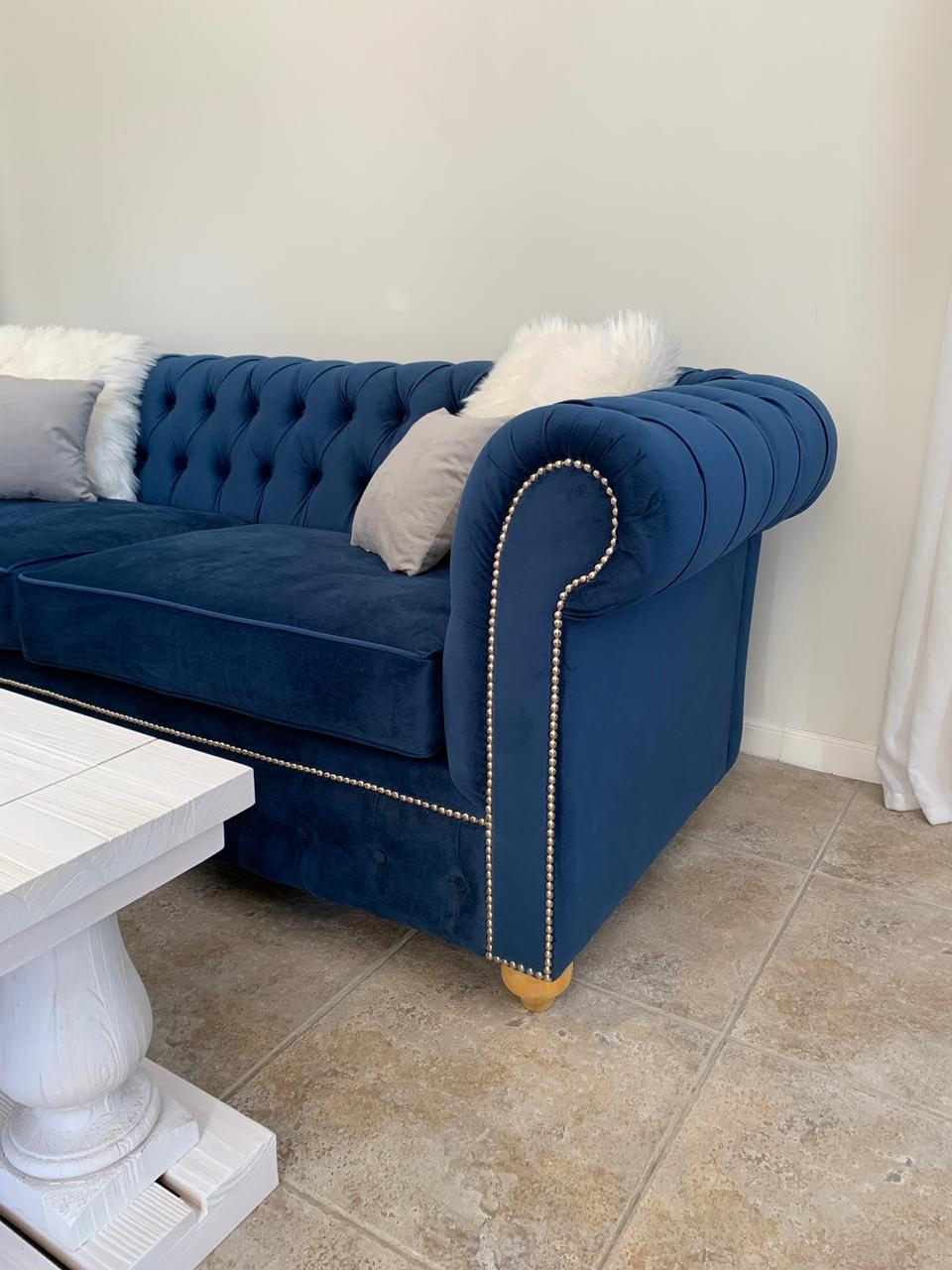 Juego de sillones con tapizado capitoné en tonos azul marino y gris, de diseño elegante y clásico, ubicados en un living luminoso con decoración sofisticada