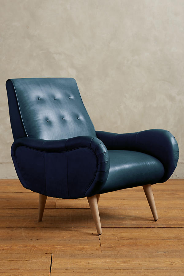 Sillón de un cuerpo estilo retro tapizado en azul, con respaldo bajo capitoné, apoyabrazos curvos y patas de madera cónicas.