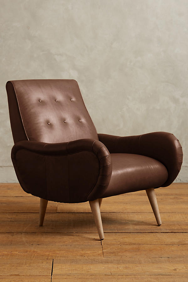 Sillón de un cuerpo estilo retro tapizado en marron, con respaldo bajo capitoné, apoyabrazos curvos y patas de madera cónicas.