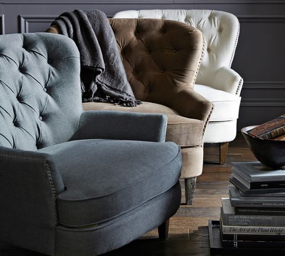 Sillón clásico tapizado con respaldo capitoné curvo, asiento acolchado y patas de madera cónicas.
