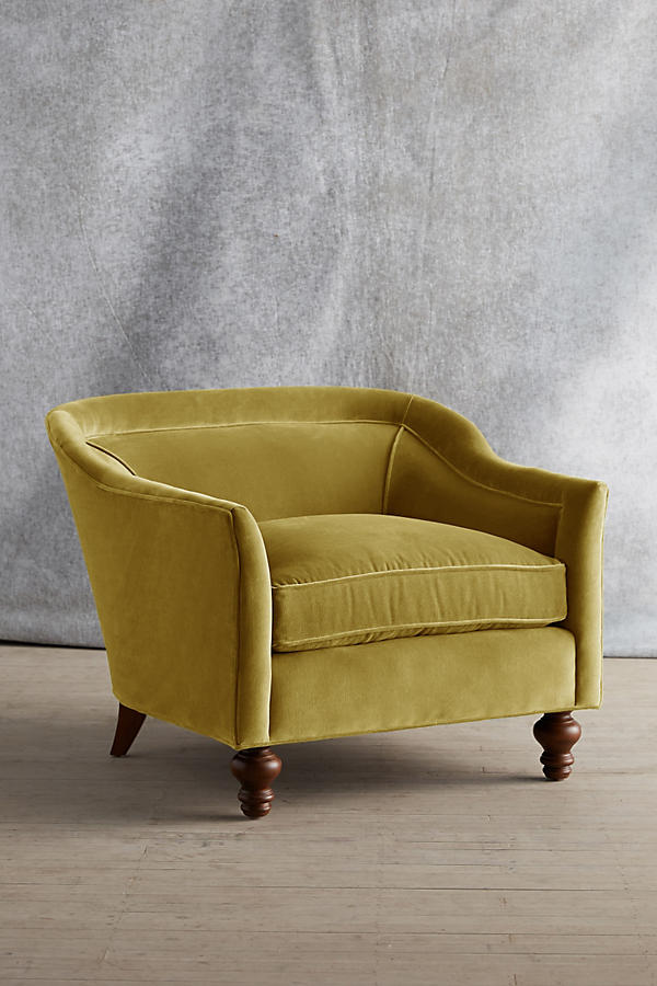 Sillón individual tapizado en color amarillo, con diseño de respaldo envolvente, asiento amplio y patas torneadas de madera oscura.