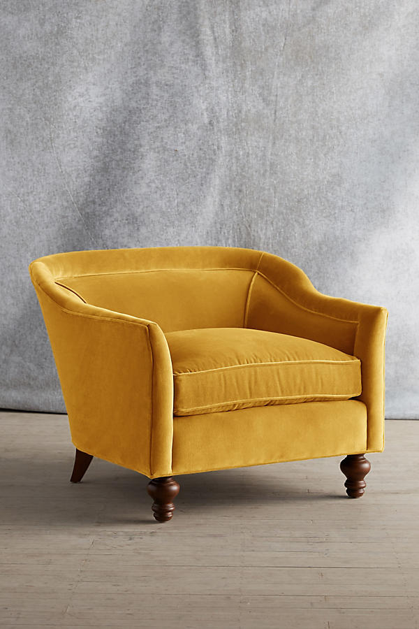 Sillón individual tapizado en color amarillo, con diseño de respaldo envolvente, asiento amplio y patas torneadas de madera oscura.