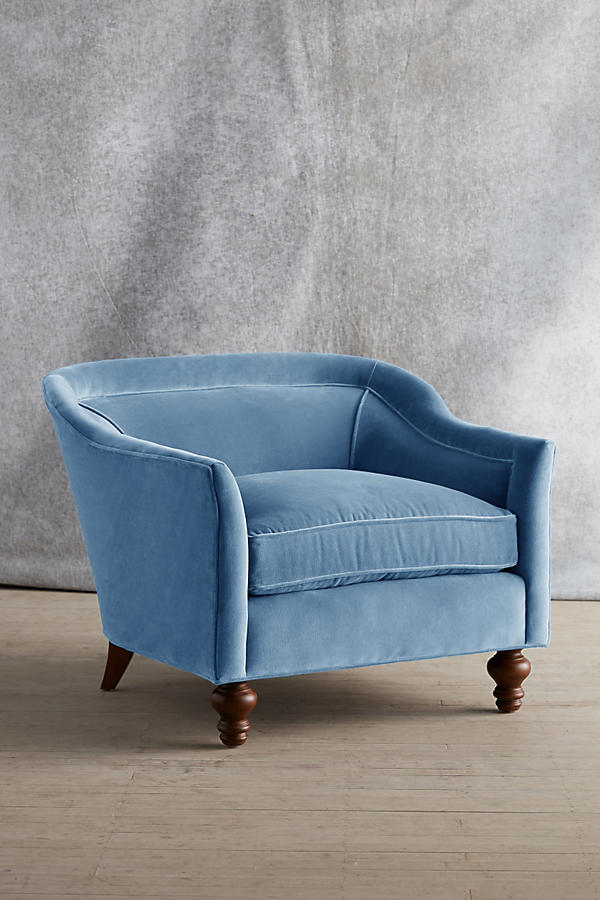 Sillón individual tapizado en color celeste, con diseño de respaldo envolvente, asiento amplio y patas torneadas de madera oscura.
