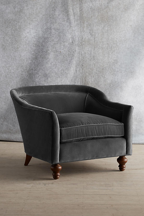 Sillón individual tapizado en color gris, con diseño de respaldo envolvente, asiento amplio y patas torneadas de madera oscura.