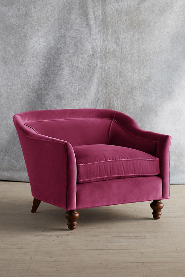 Sillón individual tapizado en color magenta, con diseño de respaldo envolvente, asiento amplio y patas torneadas de madera oscura.