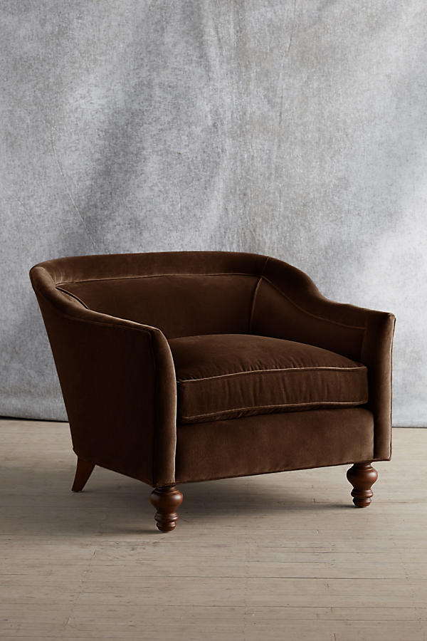 Sillón individual tapizado en color marron, con diseño de respaldo envolvente, asiento amplio y patas torneadas de madera oscura.