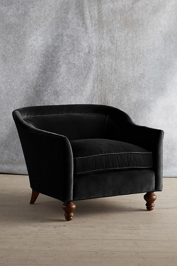 Sillón individual tapizado en color negro, con diseño de respaldo envolvente, asiento amplio y patas torneadas de madera oscura.