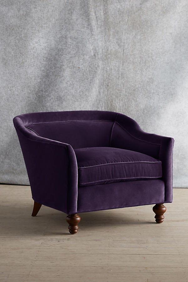 Sillón individual tapizado en color violeta, con diseño de respaldo envolvente, asiento amplio y patas torneadas de madera oscura.