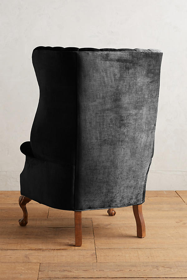 Sillón individual tapizado en negro, con respaldo alto acanalado de líneas verticales, brazos curvos y patas delanteras torneadas con ruedas pequeñas.
