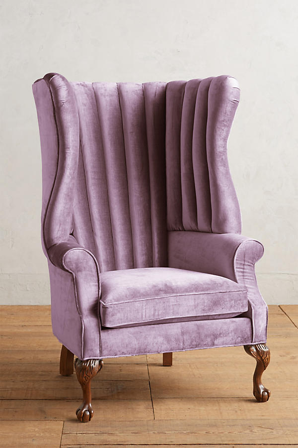 Sillón individual tapizado en violeta, con respaldo alto acanalado de líneas verticales, brazos curvos y patas delanteras torneadas con ruedas pequeñas.