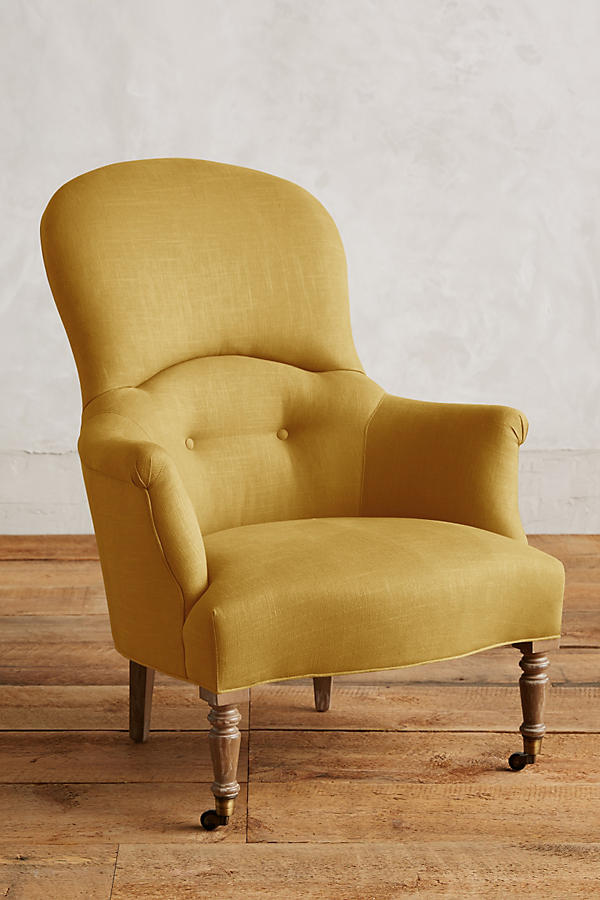 Sillón individual de diseño tradicional en tono amarillo, con respaldo curvo, apoyabrazos tallados y patas delanteras de madera con ruedas.