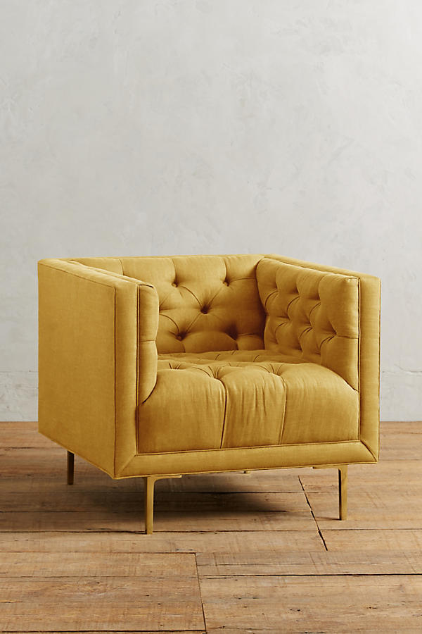 Sillón individual tapizado en amarillo, de forma cúbica con respaldo y brazos rectos, capitoné de botones en todo el interior y patas delgadas de madera.
