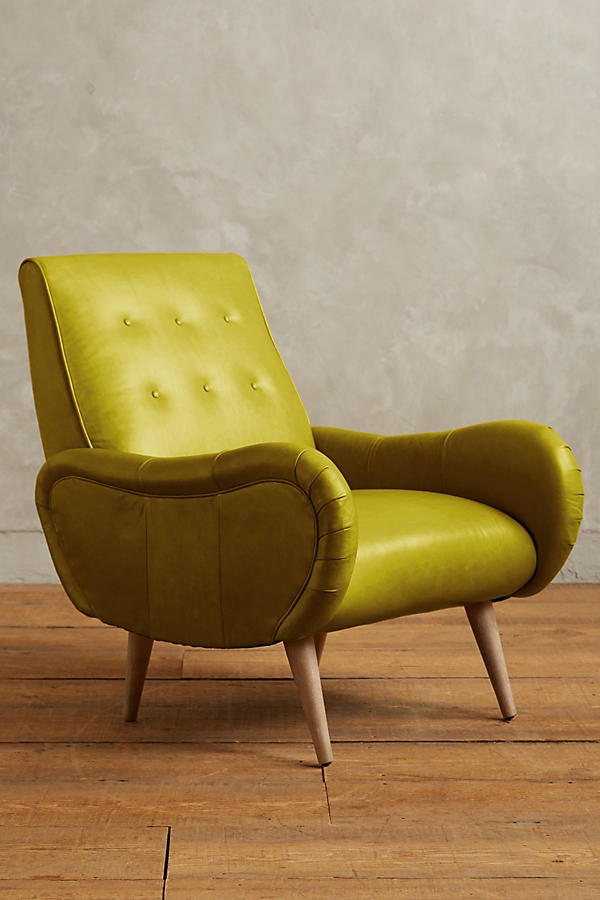 Sillón de un cuerpo estilo retro tapizado en amarillo, con respaldo bajo capitoné, apoyabrazos curvos y patas de madera cónicas.
