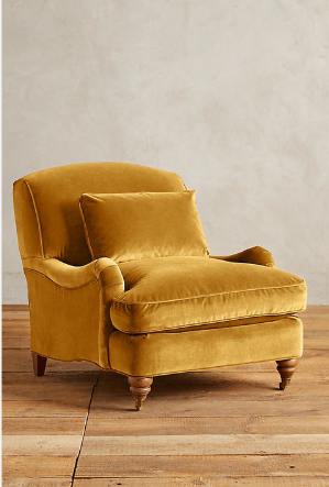 Sillón individual tapizado en amarillo, con cojín lumbar suelto, apoyabrazos curvos, respaldo levemente inclinado y patas torneadas de madera en tono medio.