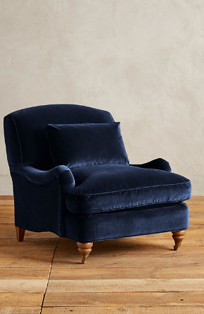 Sillón individual tapizado en azul, con cojín lumbar suelto, apoyabrazos curvos, respaldo levemente inclinado y patas torneadas de madera en tono medio.